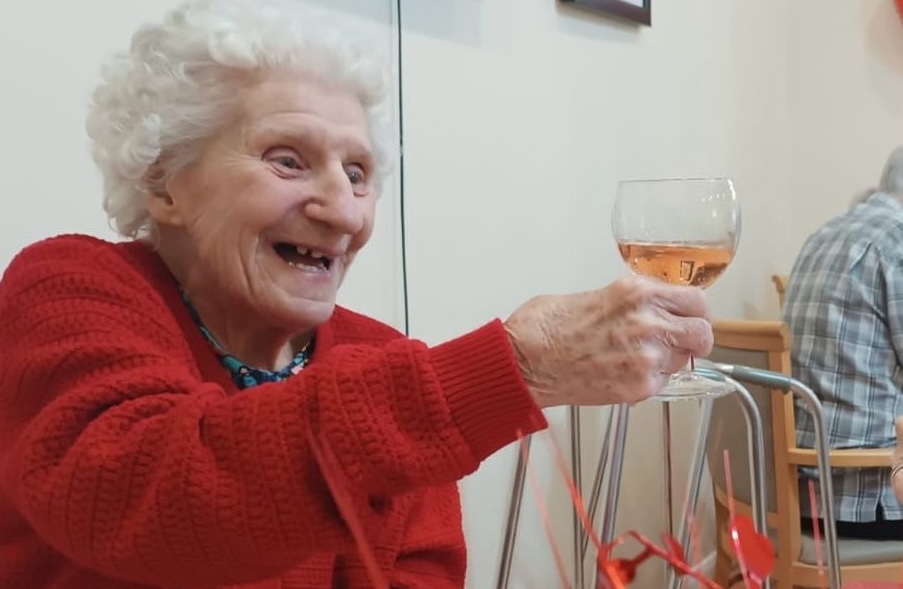 An elderly woman holding a glass of wine and smiling