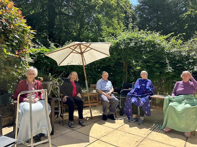 Group of elderly people sat outside in a garden under a sun shade