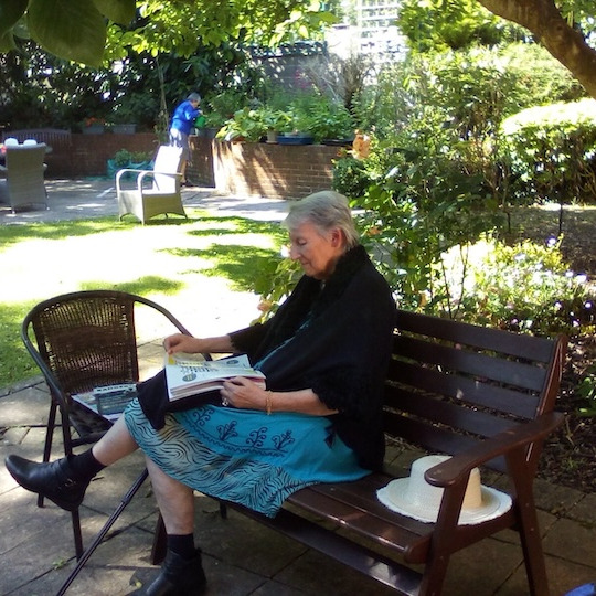 Elderly lady sat on a garden bench ready a book