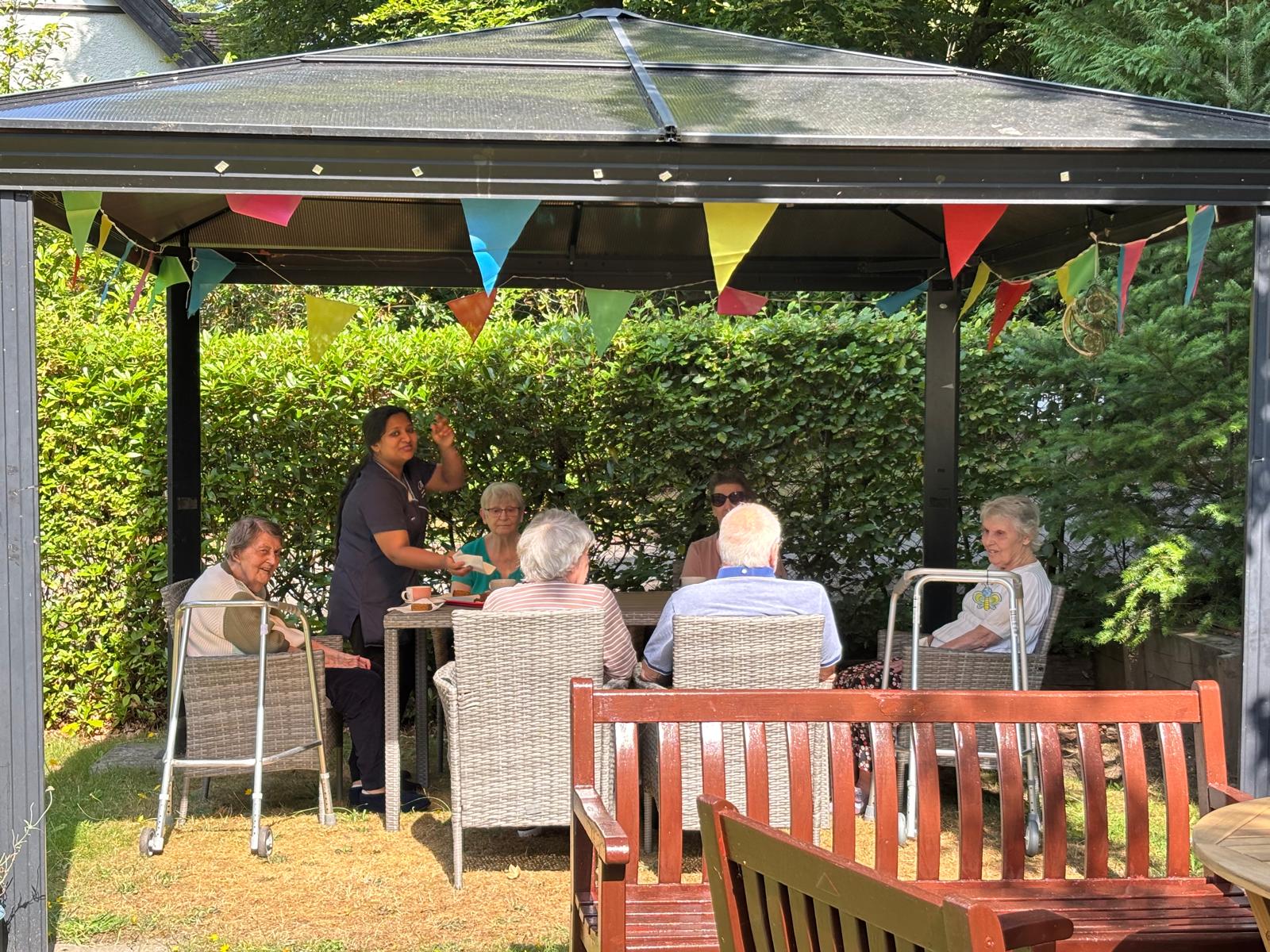 Group of elderly people sat around a table in a garden under a gazebo