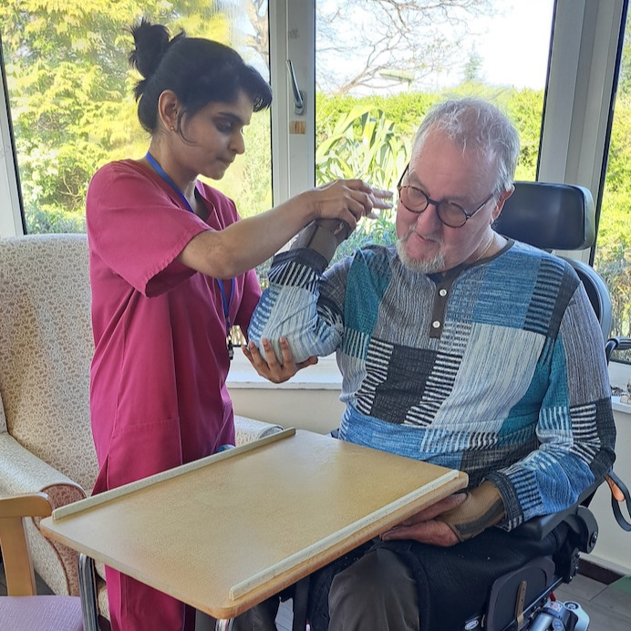 Man in wheelchair being helped to do exercises by a member of care staff