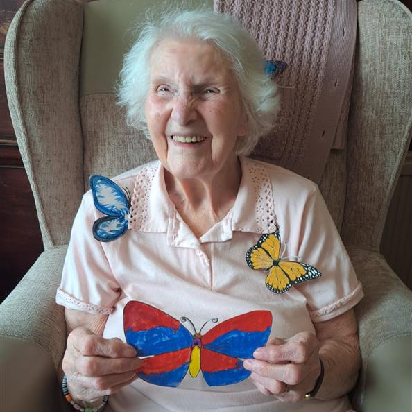 An older woman smiling widely while holding pictures of butterflies