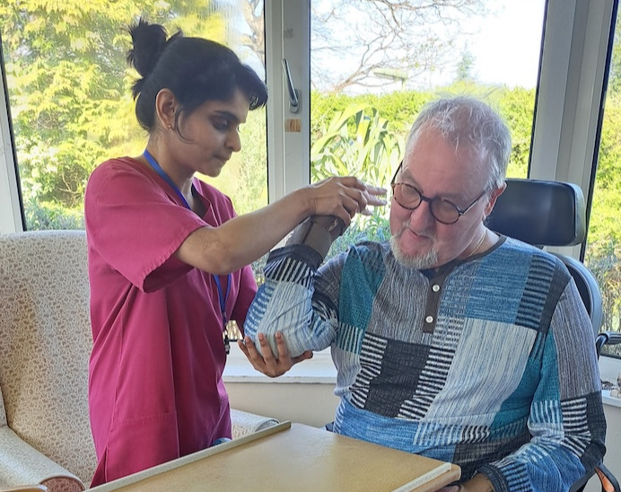 Man in wheelchair being helped to do exercises by a member of care staff