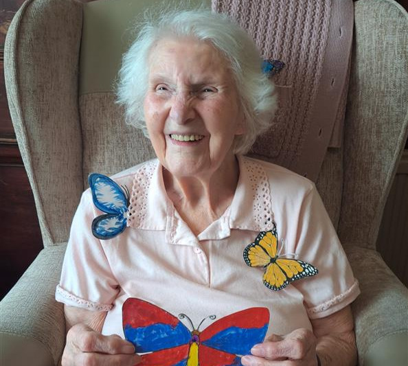 An older woman smiling widely while holding pictures of butterflies