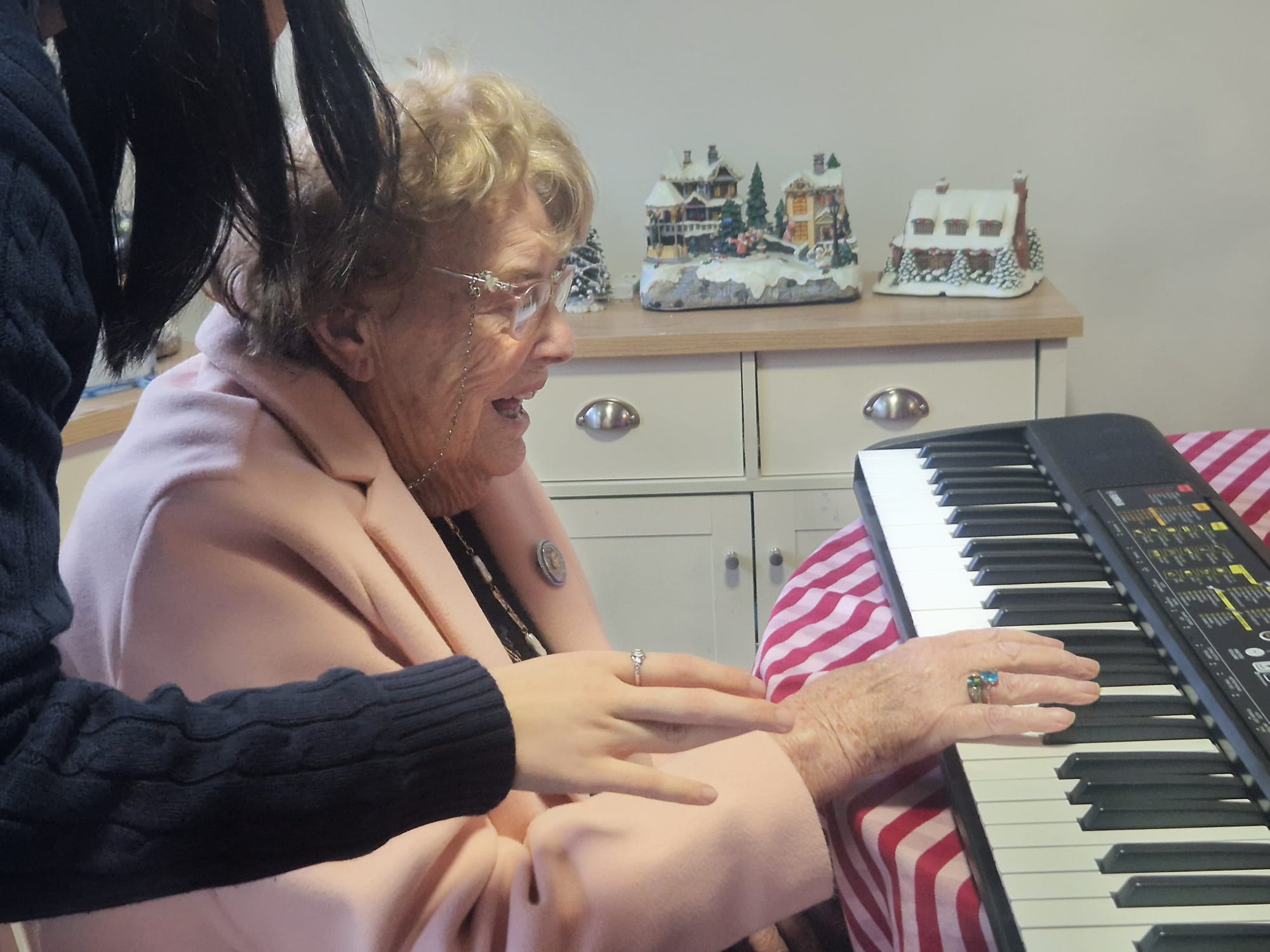 An older woman playing the piano with the help of a younger lady