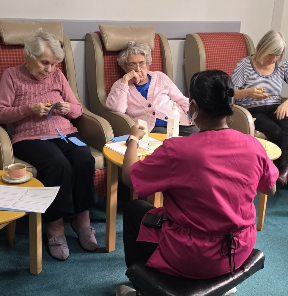 A group of residents sat in armchairs doing a creative activity with a member of staff