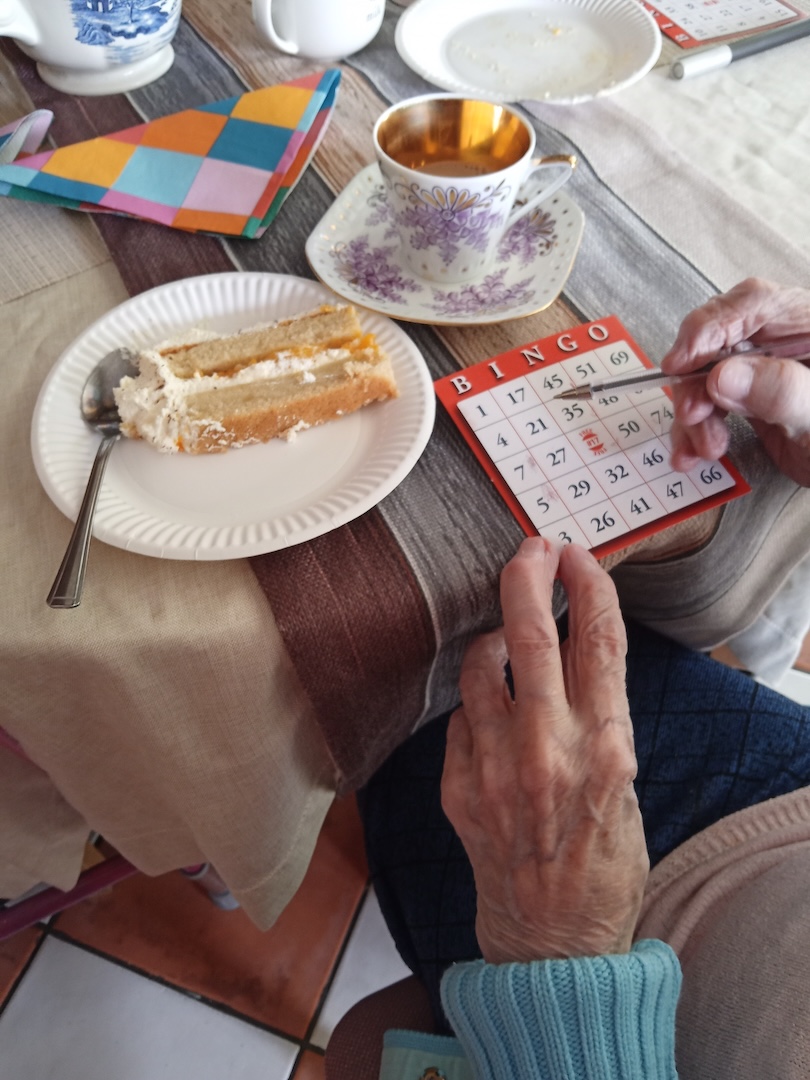 Lady's hands filling out a bingo card with a cup of tea and cake 