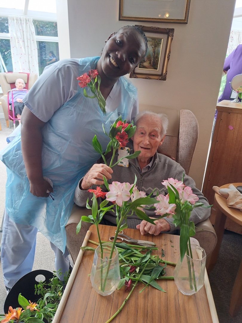 Elderly man and staff member smiling with flowers