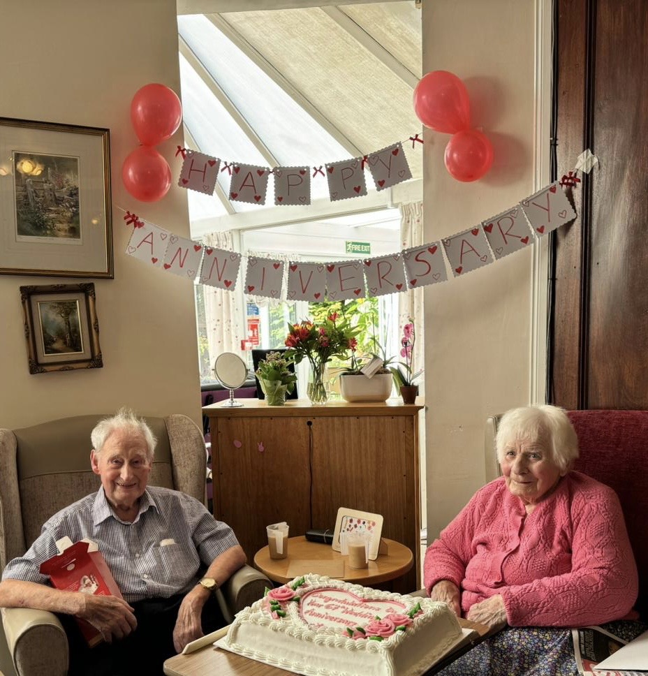 An elderly couple sat with an anniversary cake