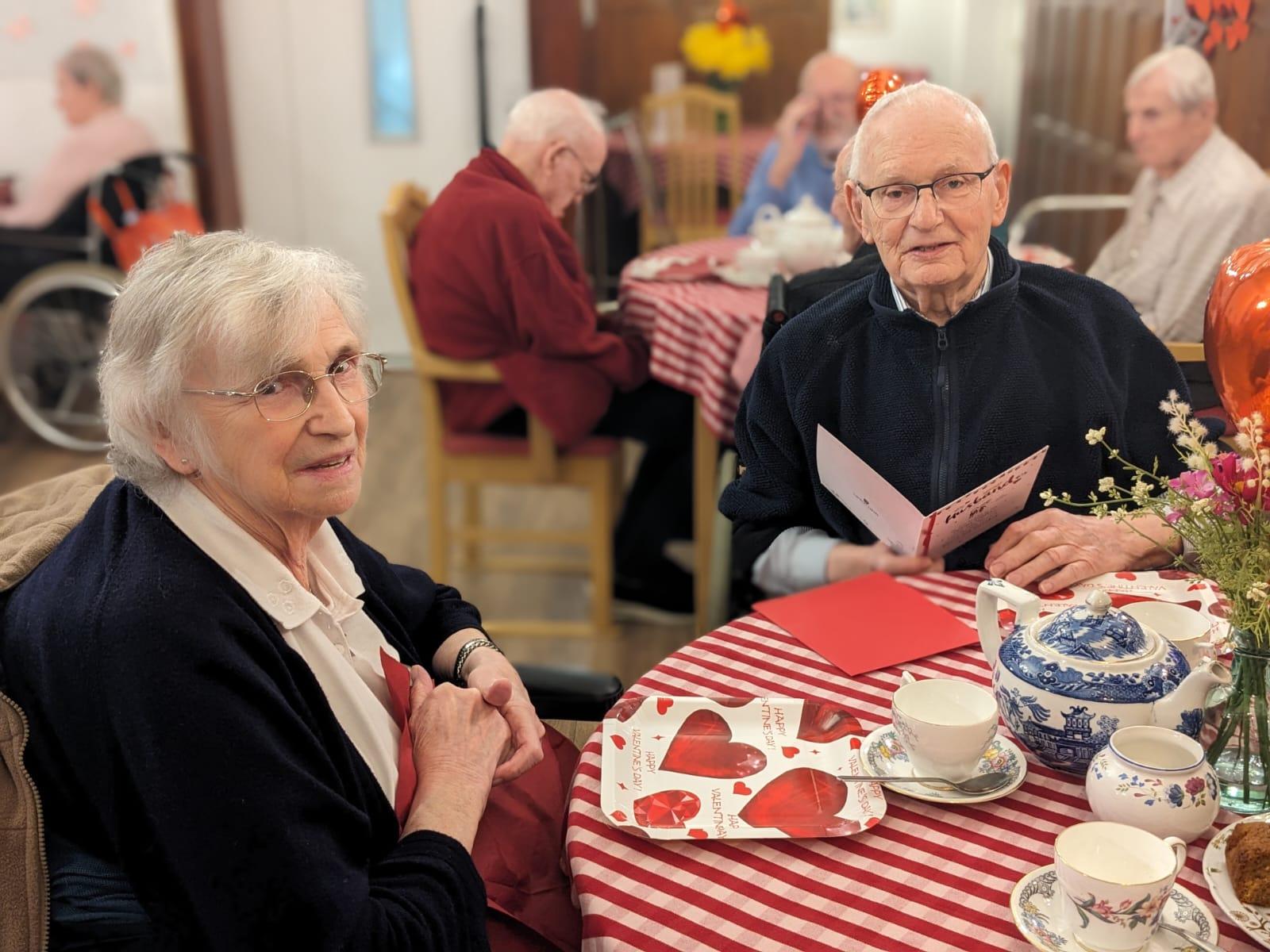 An elderly man and woman sat at a table exchanging greetings cards