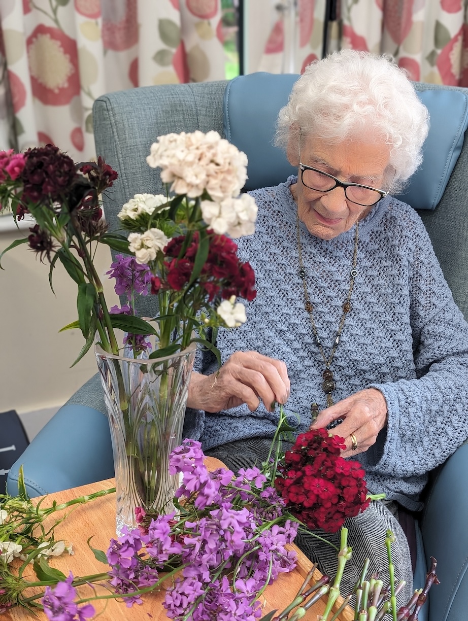 An elderly lady arranging a vase of flowers