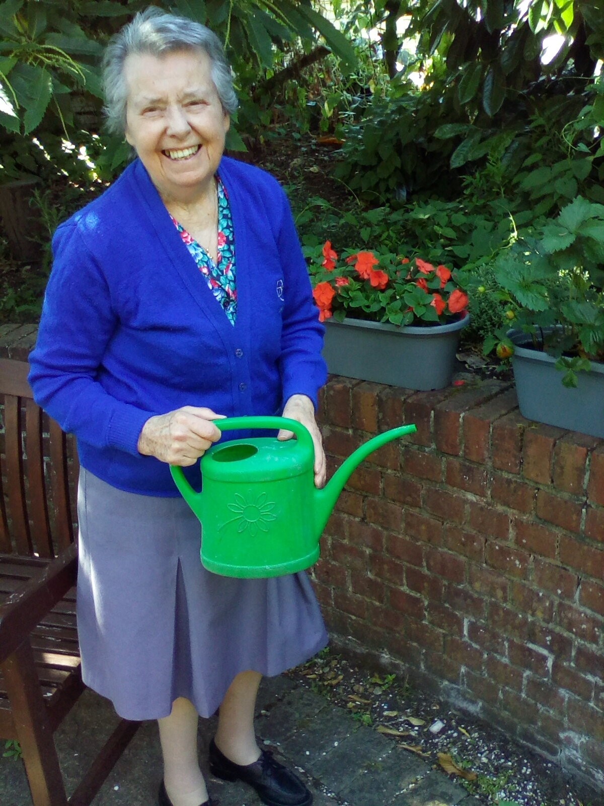 An older woman smiling holding a watering can next to some plant pots