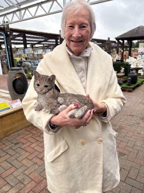 An elderly lady smiling holding a cat statue