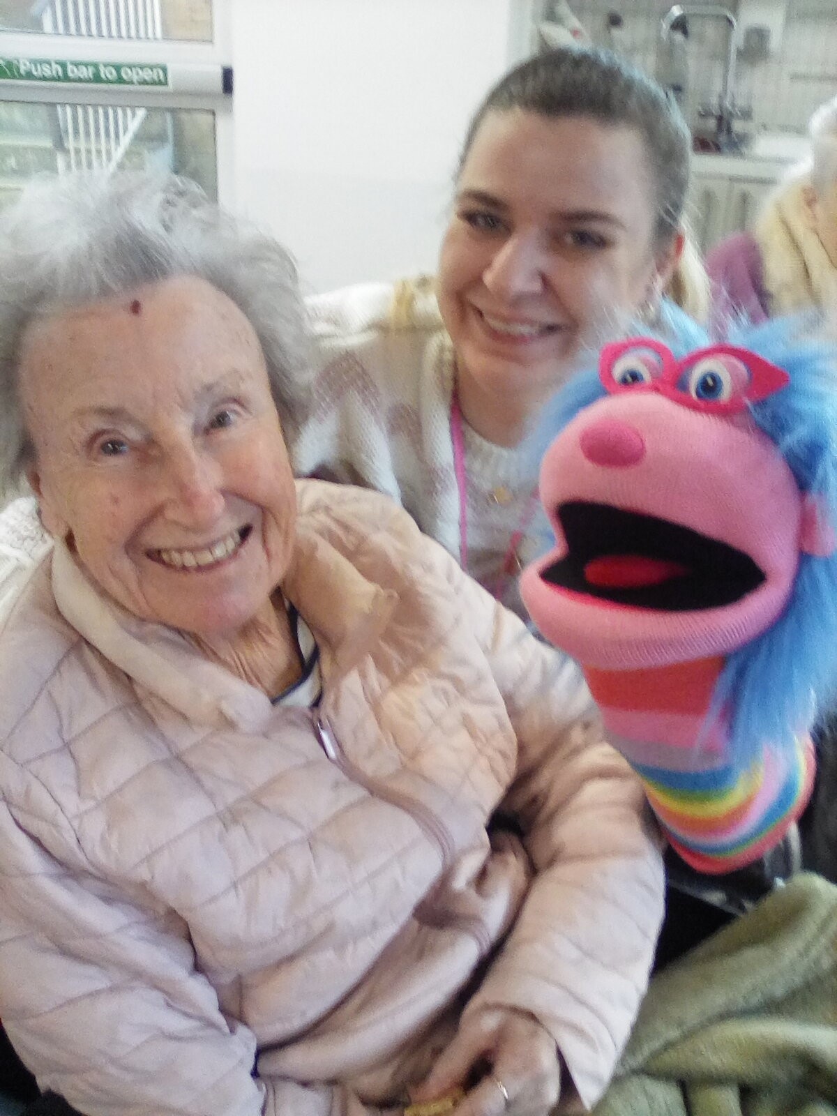 Elderly woman and staff member smiling with a puppet