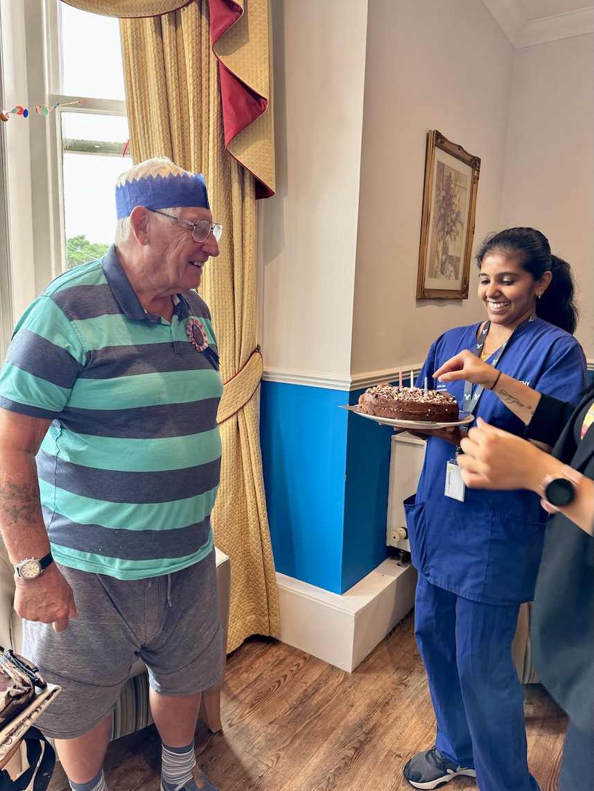 An older gentleman being presented with a birthday cake by a staff member