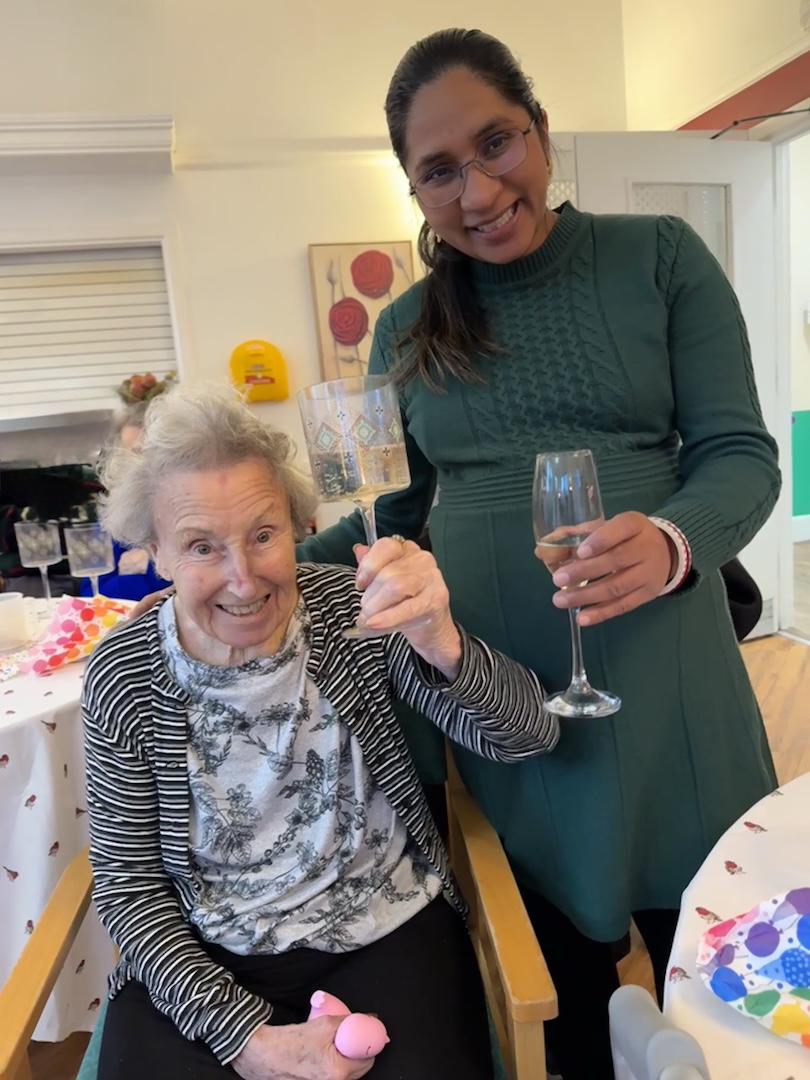 An elderly lady and member of staff holding champagne flutes
