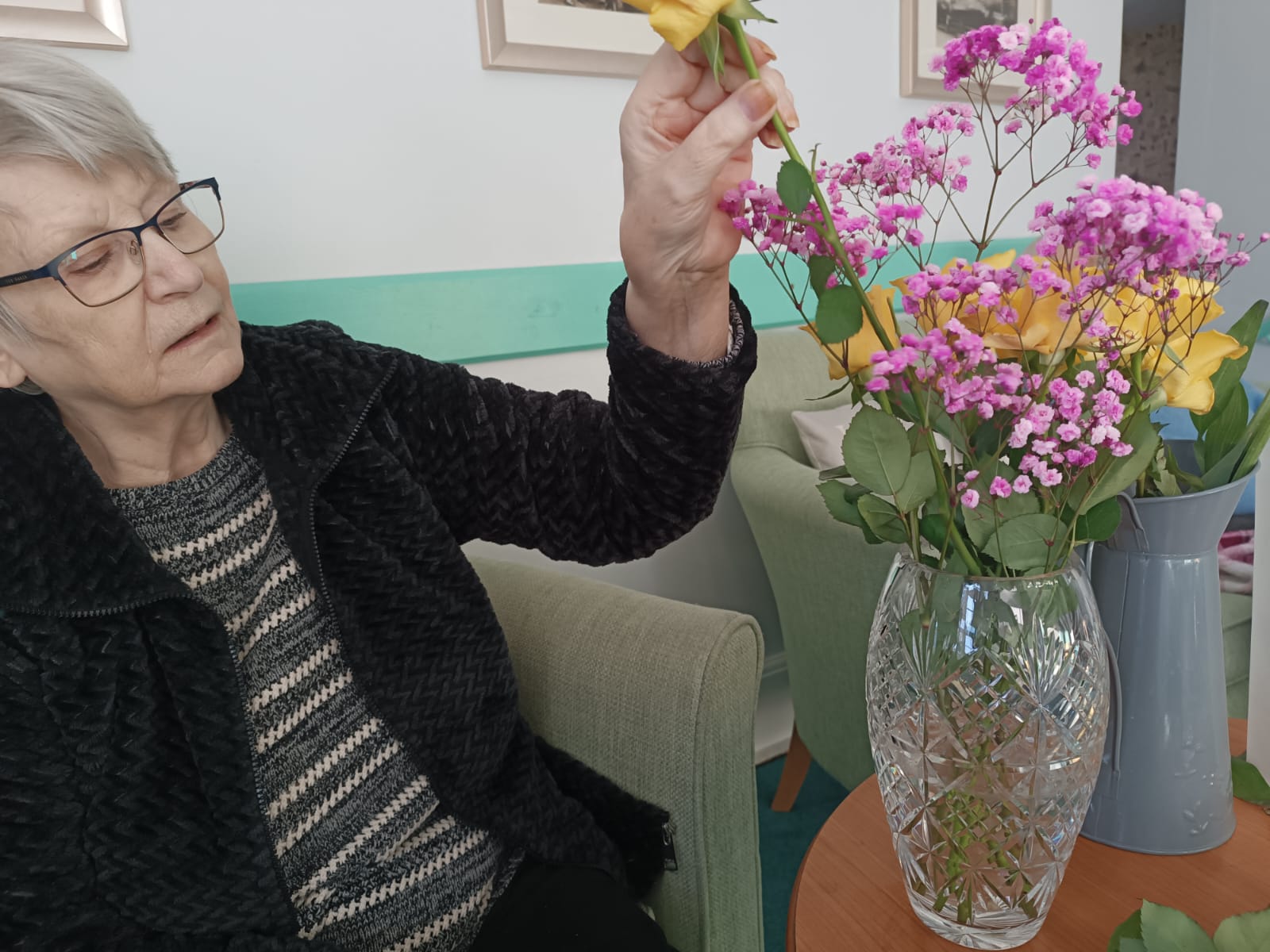 An elderly lady lady arranging a vase of flowers 