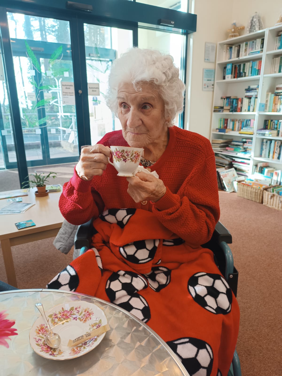 An elderly lady sat in a cafe drinking a cup of tea