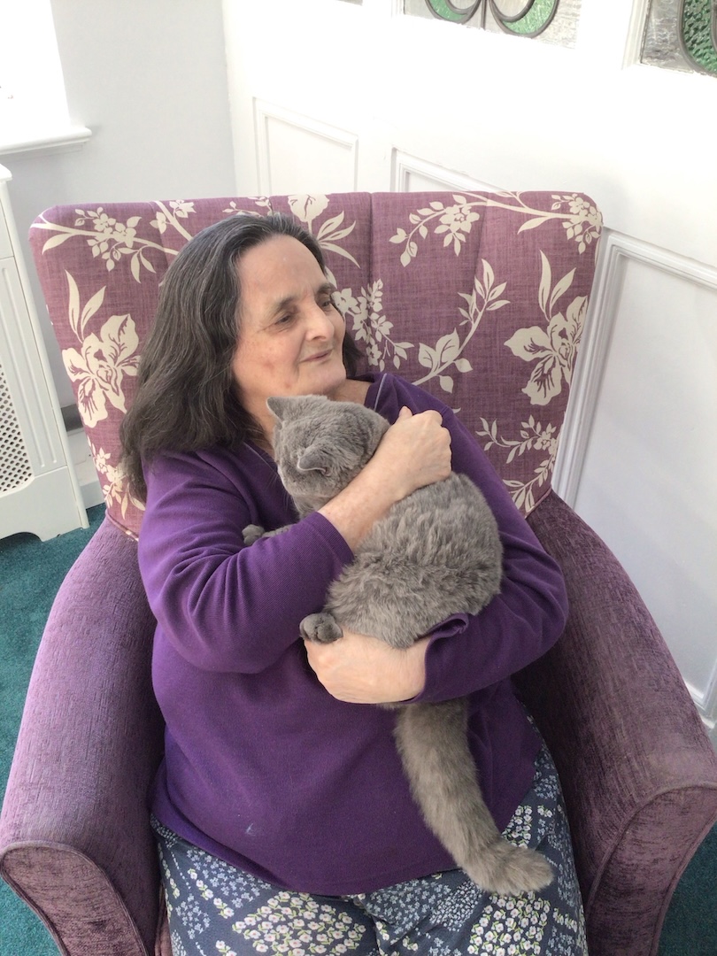 An older lady sat on an armchair cuddling a cat