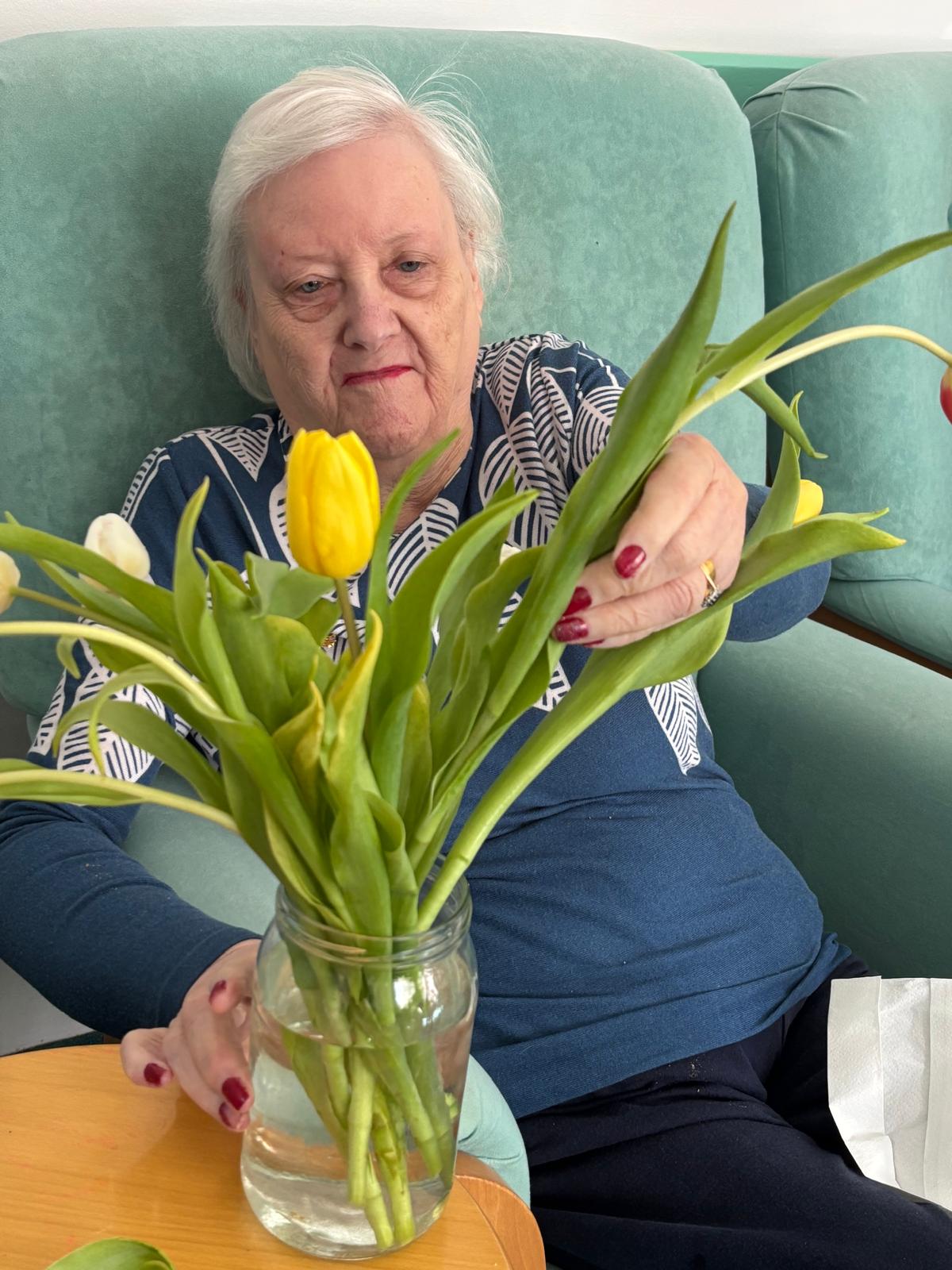 An older lady sat arranging a vase of flowers