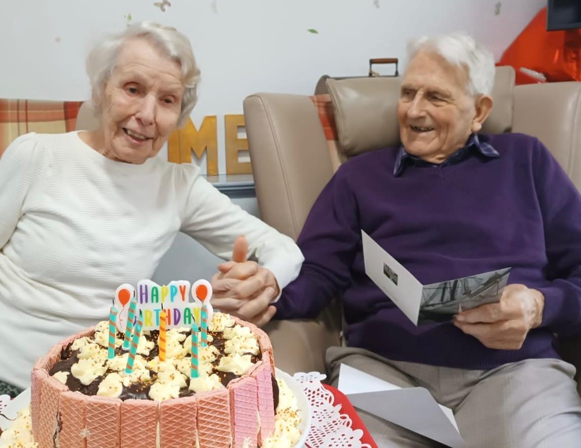An elderly couple holding hands and smiling with a birthday cake 