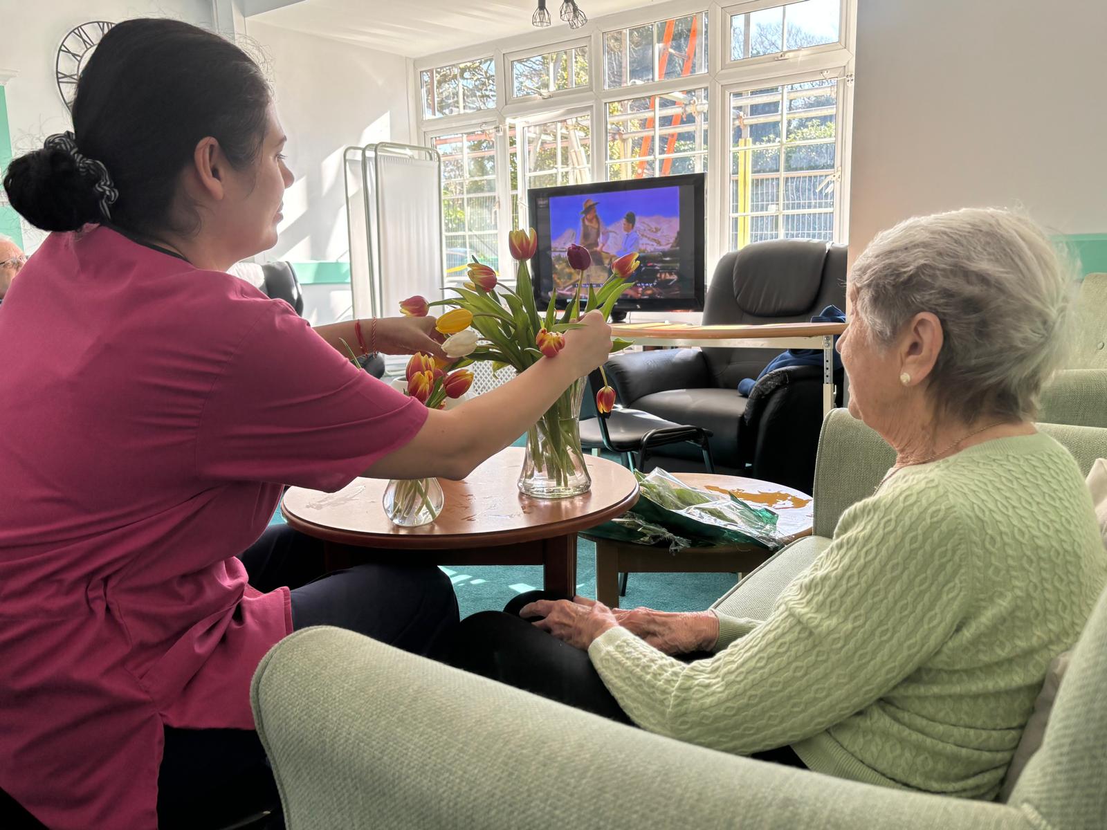 An older lady and staff member arranging a vase of flowers