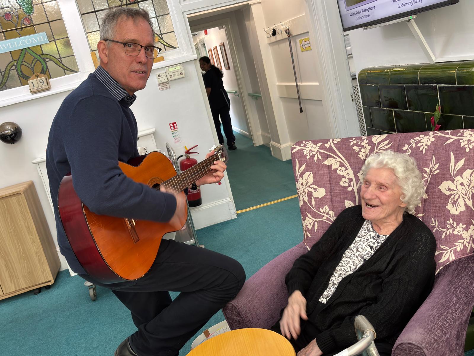 A man playing the guiter for an elderly lady sat in a chair