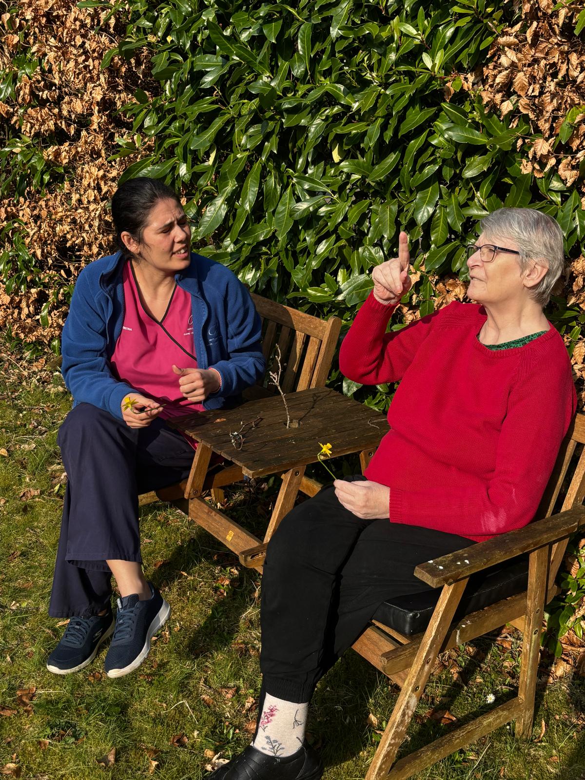 A staff member and elderly lady sat in the garden talking