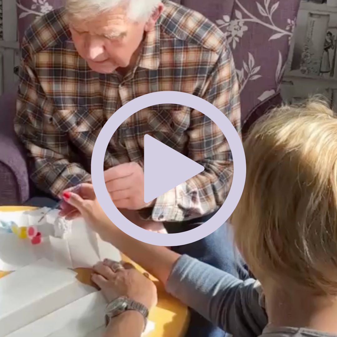 An elderly gentleman and staff member painting a picture together