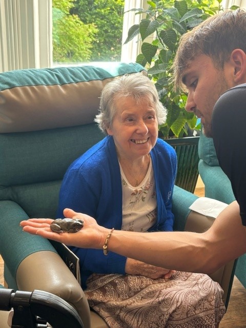 A man holding a frog out to show to an elderly lady
