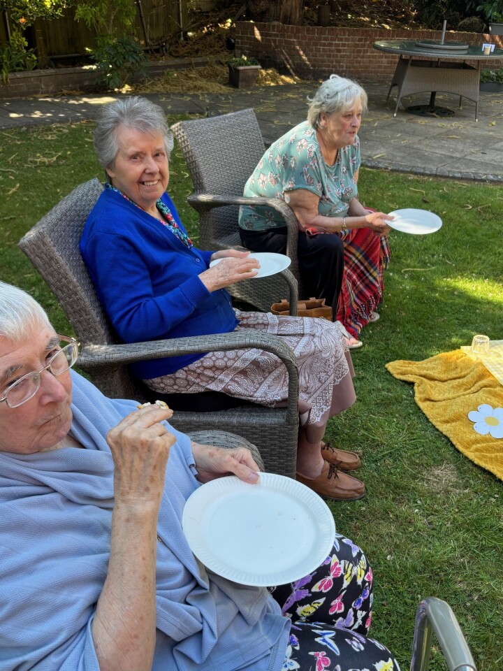 Three older women sat eating in the garden on a sunny day