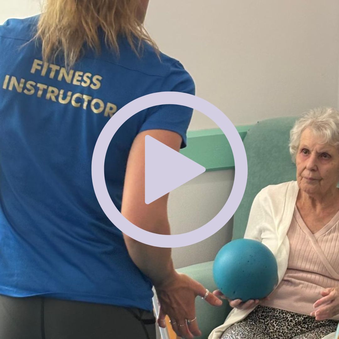An older woman participating in exercises with a ball with the help of an instructor