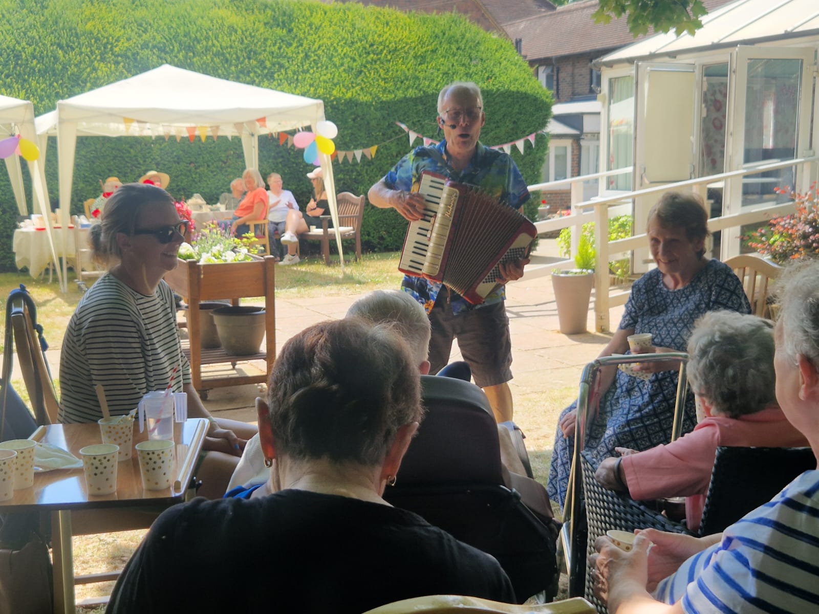 A group of people at a garden party listening to a musician play
