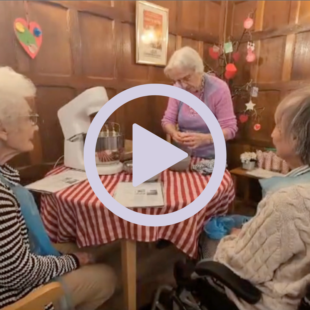 Three elderly women sat around a table baking a cake