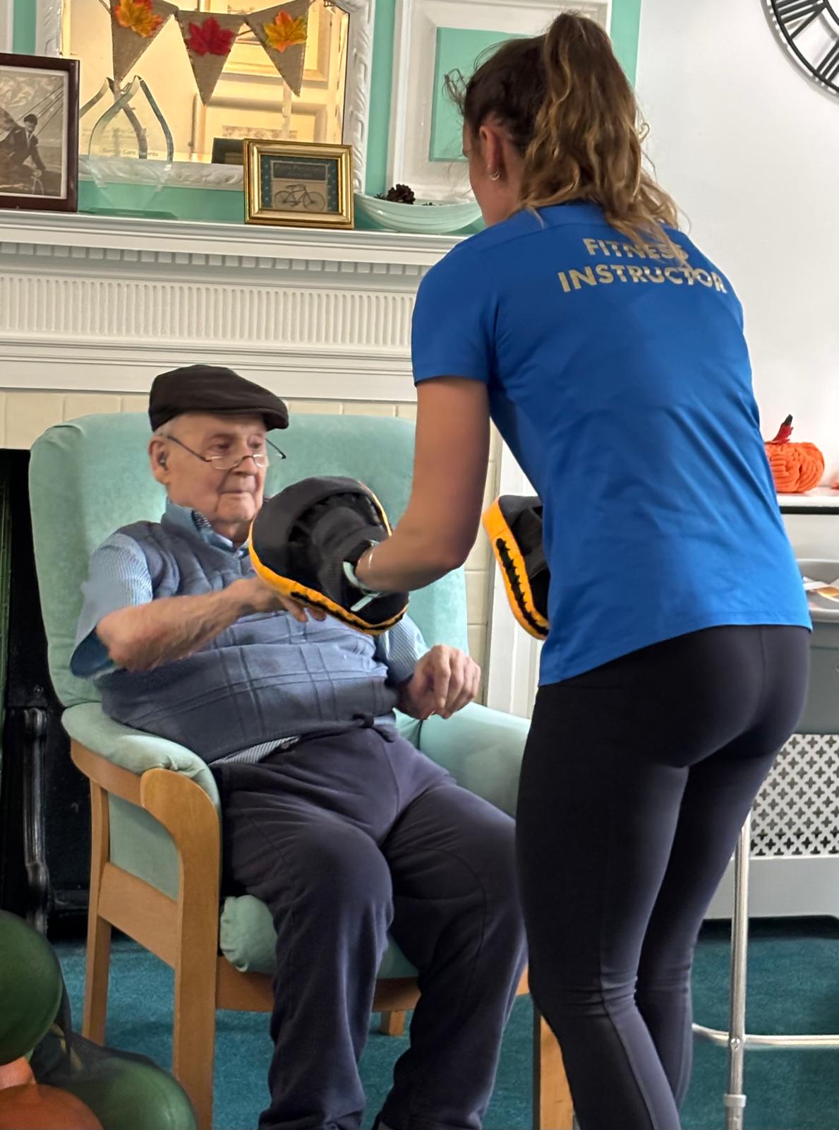 A fitness instructor helping an elderly man with exercises from his chair