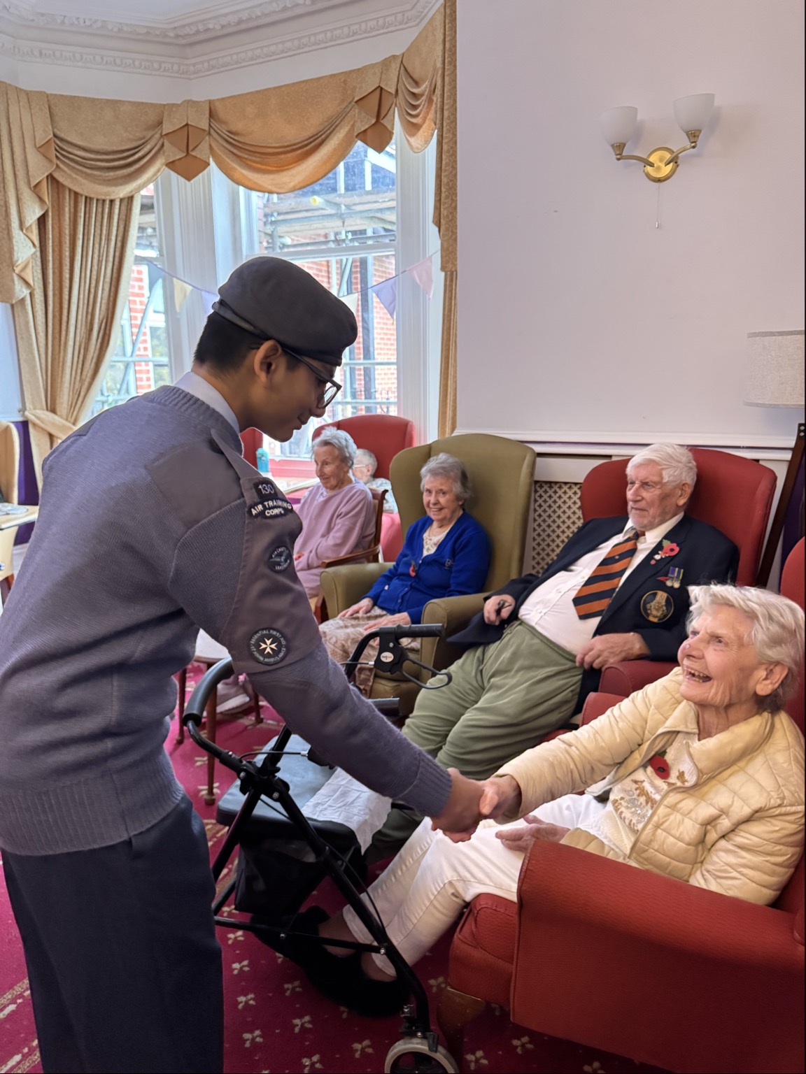 A cadet in uniform shaking the hands of older people sat in armchairs