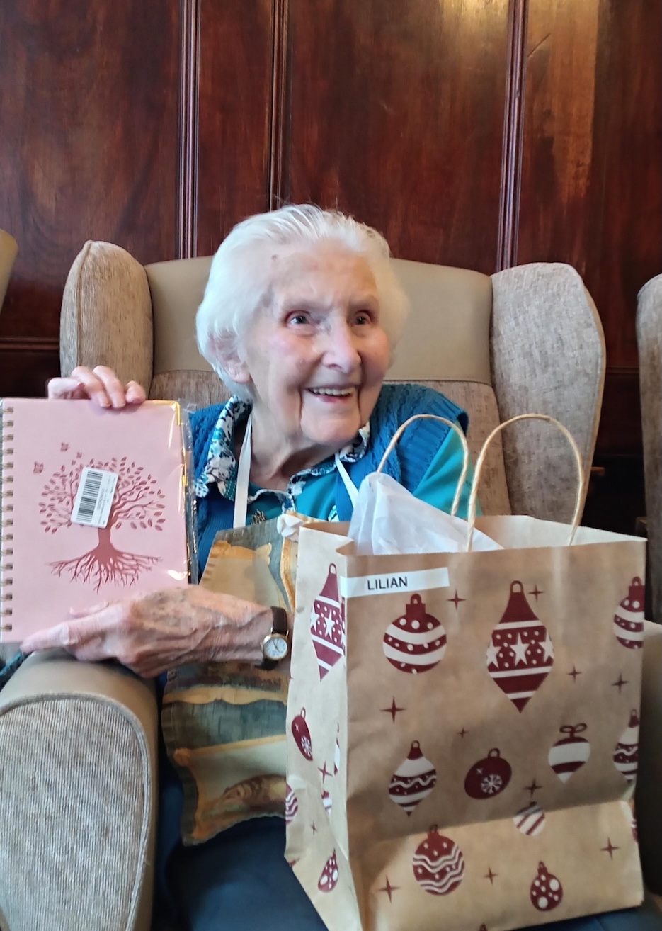 An older woman smiling while opening a Christmas gift