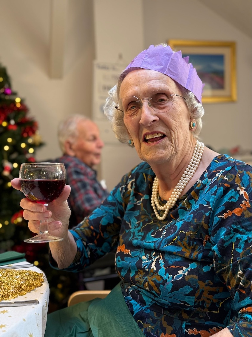 An older woman wearing a paper crown and holding a glass of wine