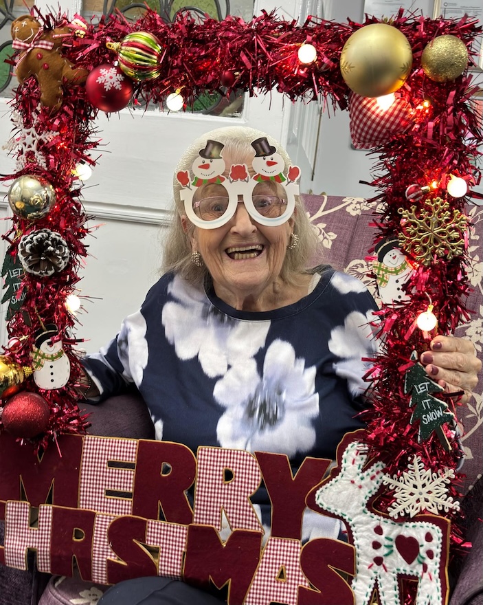 An older woman holding wearing glasses posing with a Christmas photo props