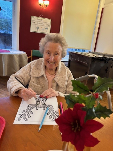 An elderly woman smiling while colouring in a Christmas picture