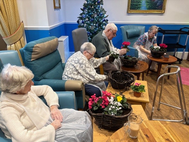 A group of people sat planting flowers in baskets indoors
