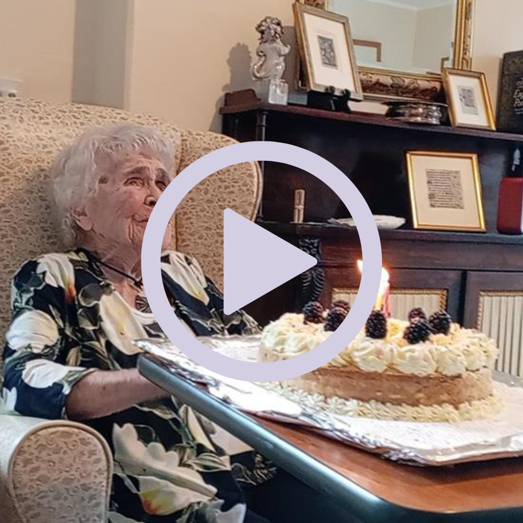 An older woman sat with a birhtday cake with candles