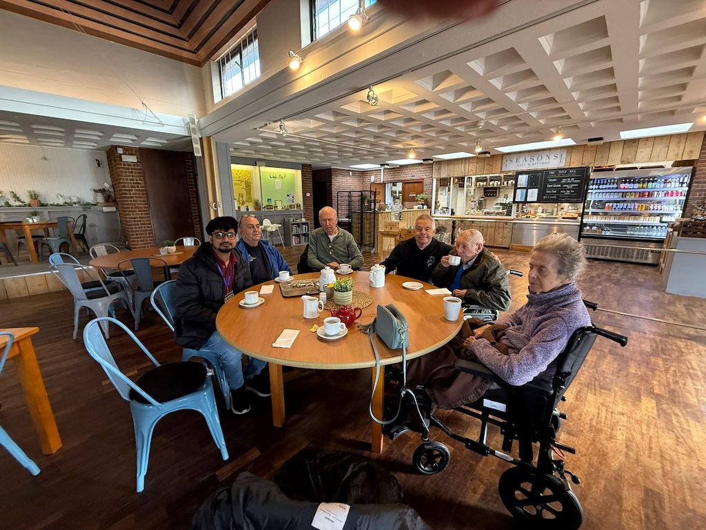 A group of people sat around a large round table drinking cups of tea