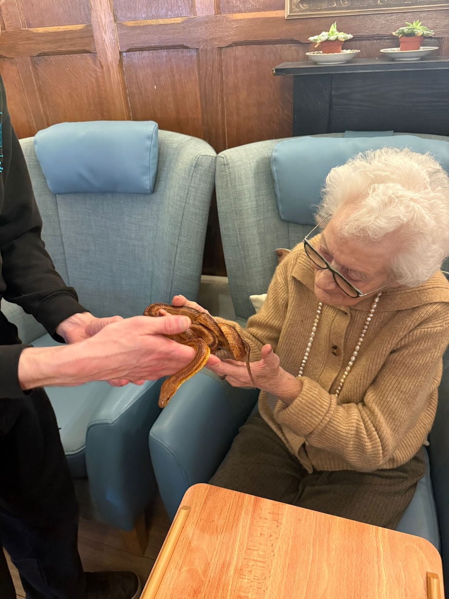 An older woman being handed a snake