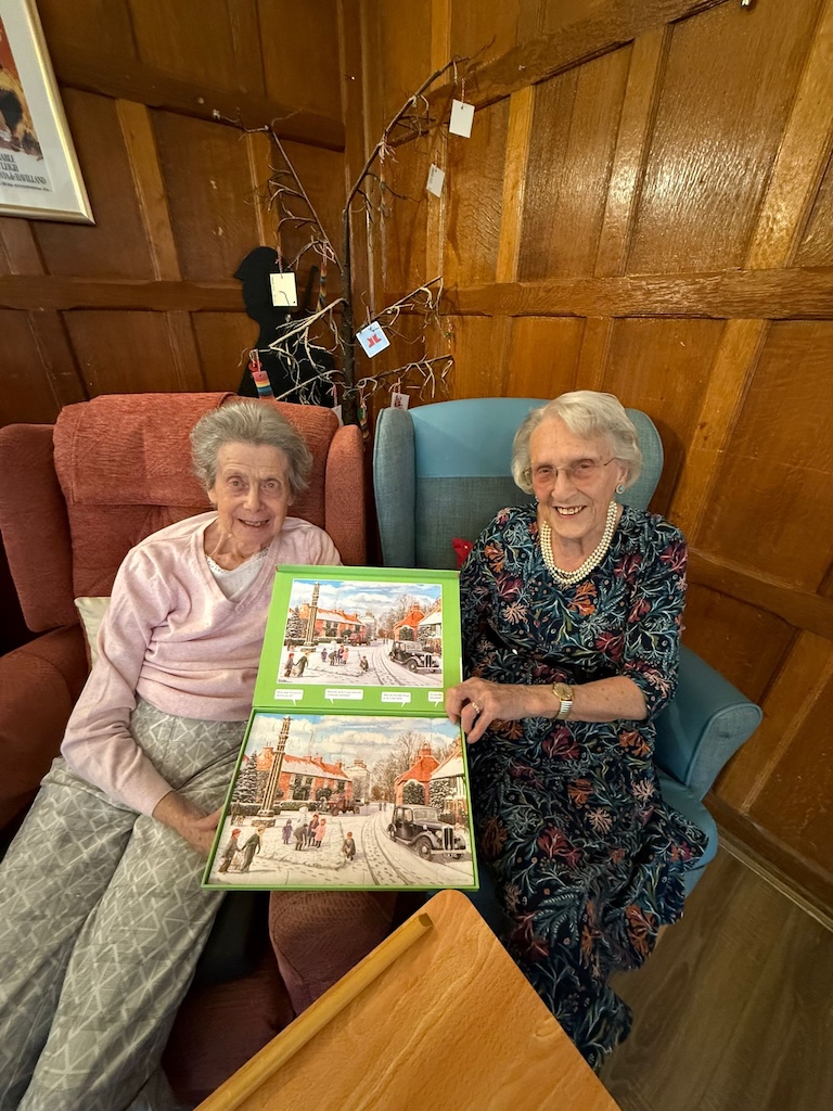 Two elderly ladies smiling holding a puzzle 