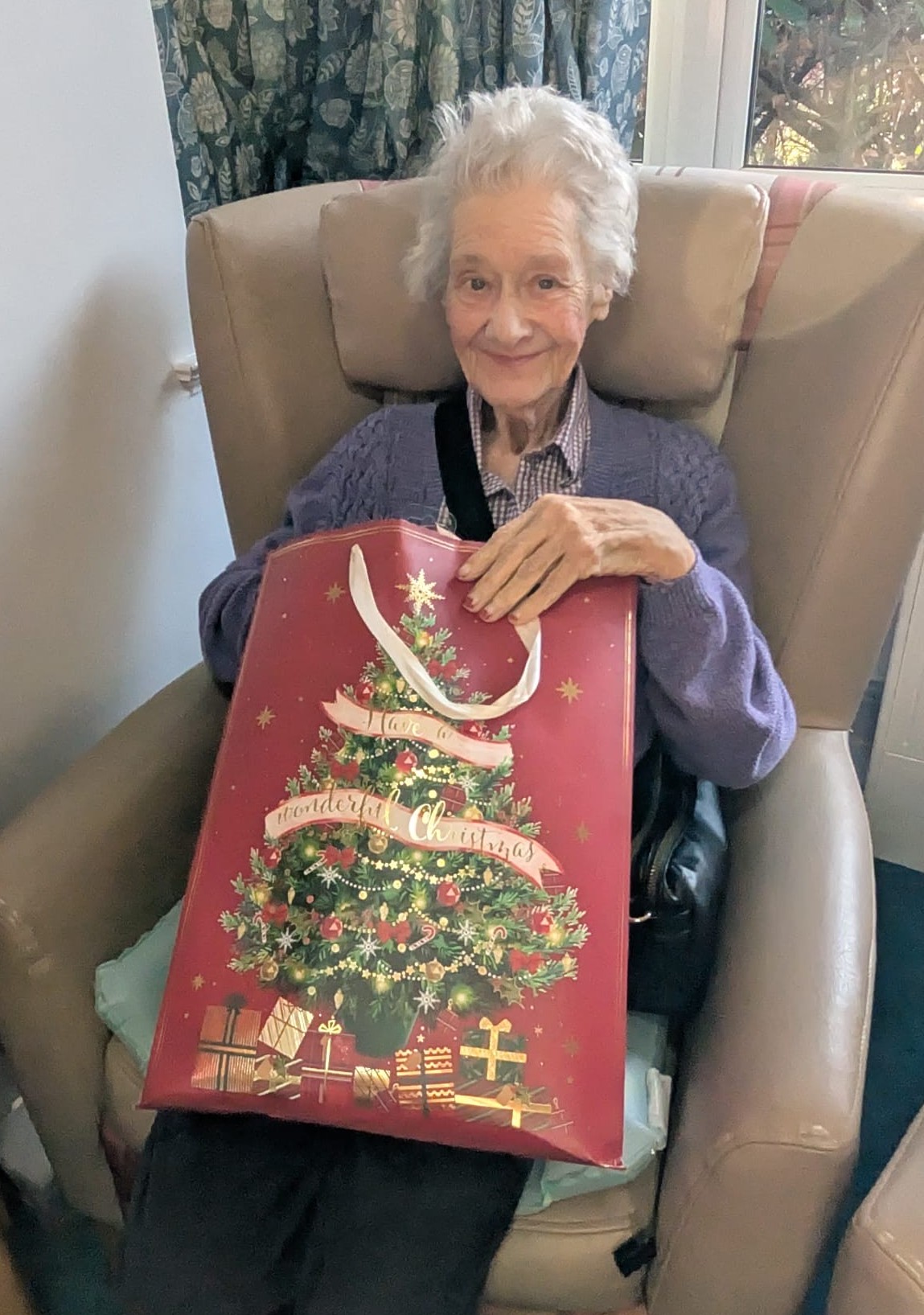 An older woman sat on an armchair opening a Christmas present