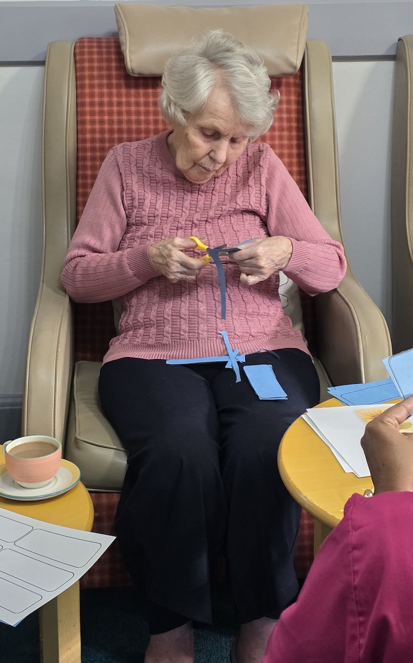 An older woman sat in a chair doing a craft activity