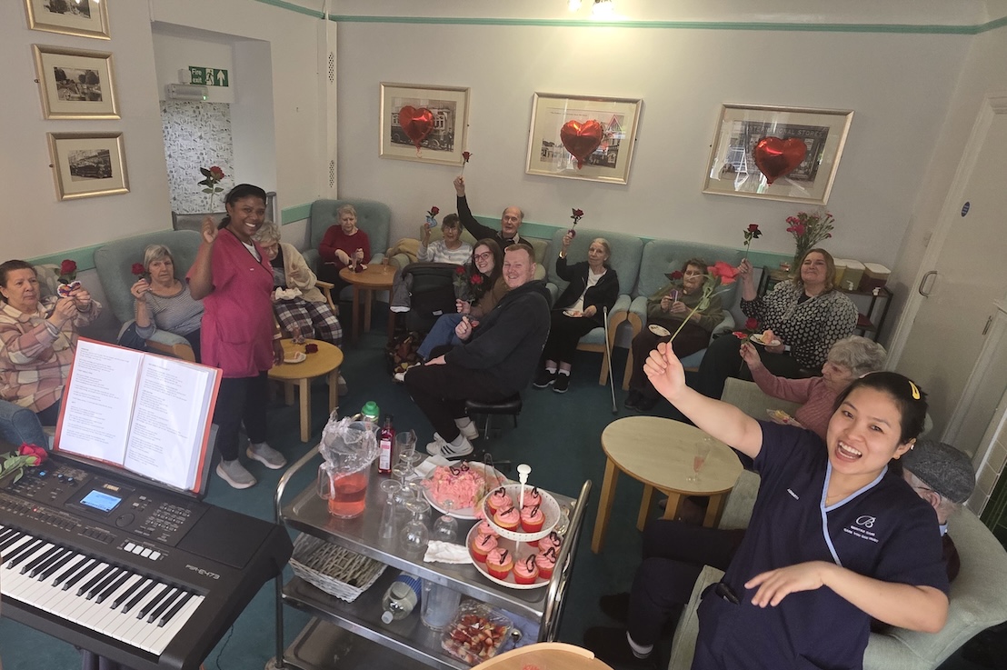 A group of people in a lounge enjoying a party and waving at the camera