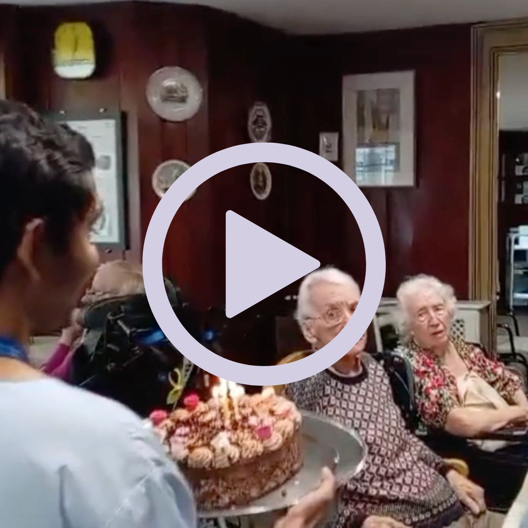 A staff member carrying a birthday cake to residents sat around a table