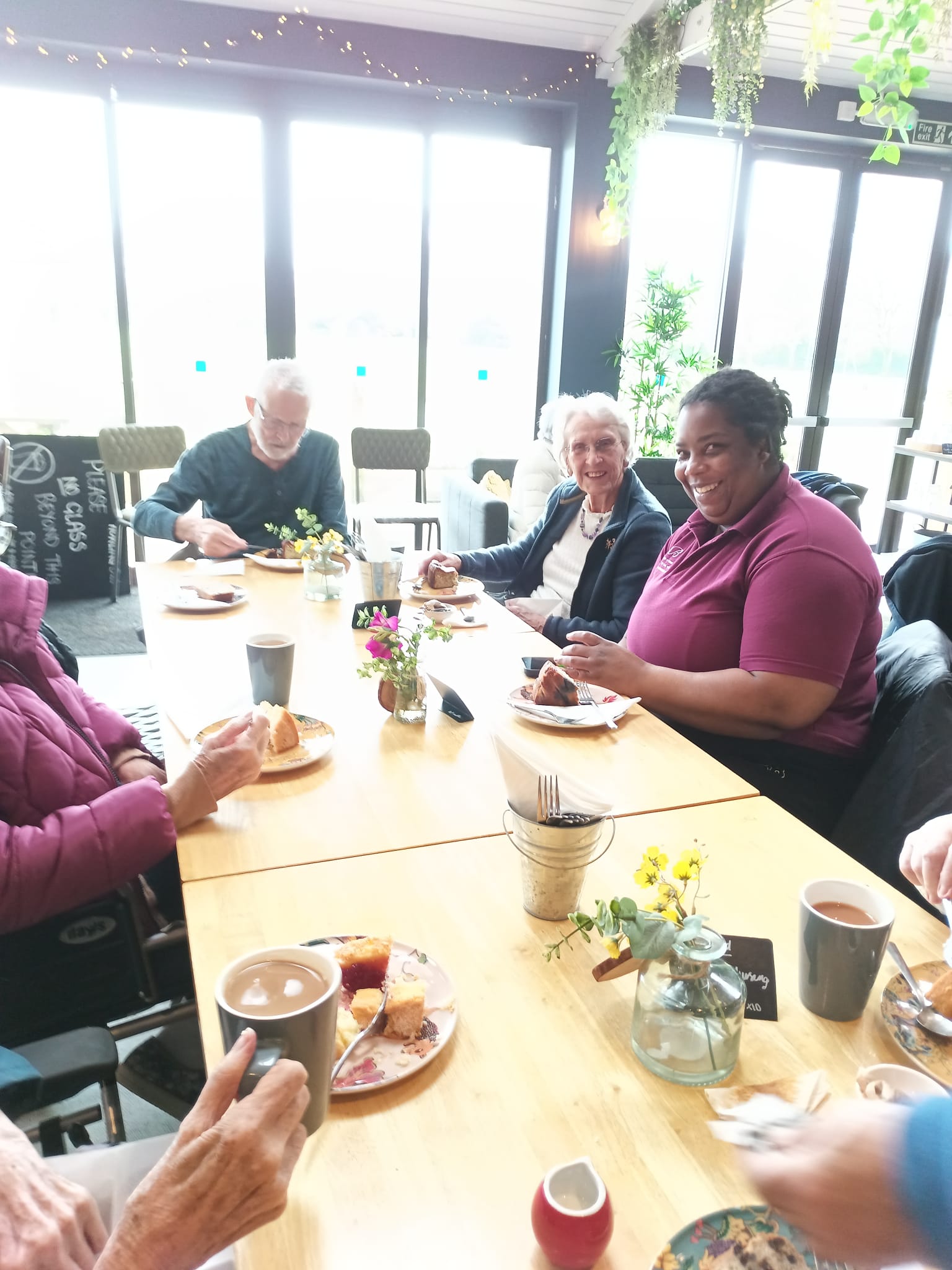 A group of people smiling sat around a table with cups of tea and cake